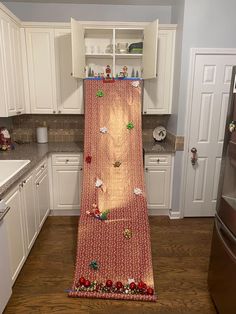 a kitchen with white cabinets and wooden flooring has a red rug hanging from the wall