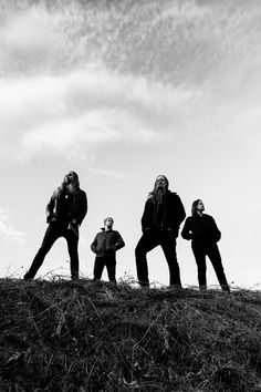 four men standing on top of a grass covered hill next to each other in black and white