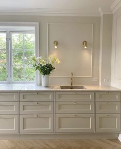 an empty kitchen with white cabinets and gold hardware on the countertop, along with a vase filled with flowers