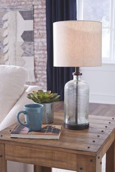 a table with a lamp, coffee cup and book on it next to a couch