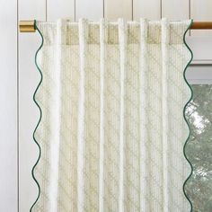 a white curtain with green scalloped trim hanging from a wooden window sill