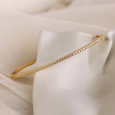 Our Classic Diamond Tennis Bangle is a dainty gold piece adorned with sparkling pavé stones, exuding elegance and sophistication. Perfect for any occasion, this versatile bracelet can be worn alone for a subtle touch of glamour or stacked with other bracelets for a classy, layered look ♡ SKU: RR-BR065 Product Details Material: 18K Gold Over Brass Finish: 18K Gold Featuring ~2.5mm wide Diamond Bangle Bracelet with CZ Pavé Diamond Stones Featured Styles Part of our Diamond & Pavé Collection Model