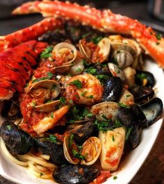 a white plate topped with pasta covered in clams and shrimp next to a lobster