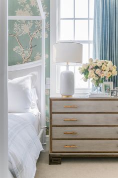 a bedroom scene with focus on the dresser and flowers in the vase next to the bed