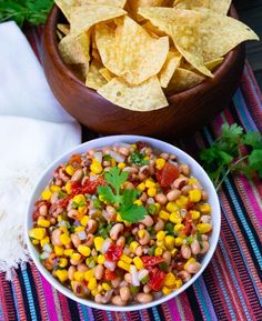 a white bowl filled with corn and salsa next to a wooden bowl full of tortilla chips