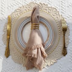 a place setting with napkins and goldware on a white lace tablecloth,