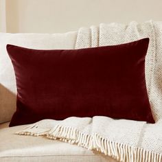 a red pillow sitting on top of a couch next to a white blanket and pillows