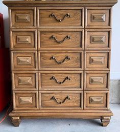 an old wooden dresser with many drawers and knobs on the front, next to a red trash can