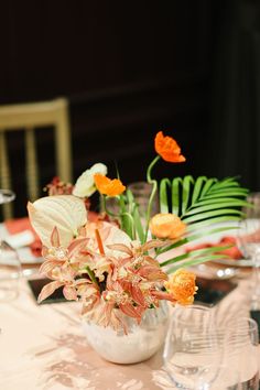 an arrangement of flowers and greenery in a vase on a table with place settings