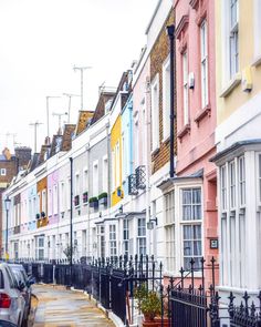 a row of houses with cars parked on the street in front of them, all painted different colors