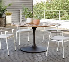 an outdoor table and chairs on a deck with potted plants in the back ground