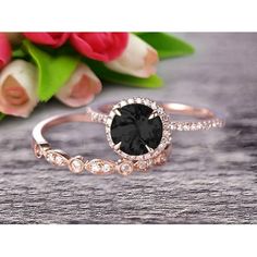 a black diamond ring sitting on top of a wooden table next to pink flowers and tulips