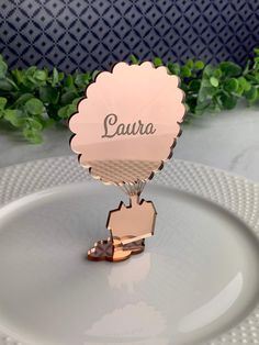 a white plate topped with a pink place card holder and a green plant in the background