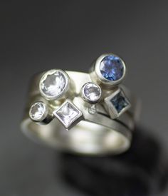 two rings with different colored stones on top of each other, one is white gold and the other is silver