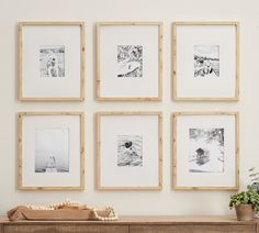 six framed photographs hang on the wall above a wooden table with a phone and potted plant