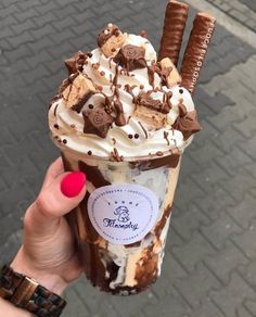 a person holding up a chocolate milkshake with whipped cream and cookies on top