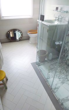 a bathroom with a walk in shower next to a white toilet and yellow stools