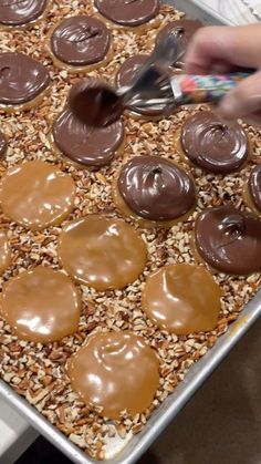 someone spreading chocolate on top of peanut butter covered pretzels in a baking pan