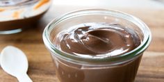 a jar filled with chocolate pudding next to a spoon on top of a wooden table