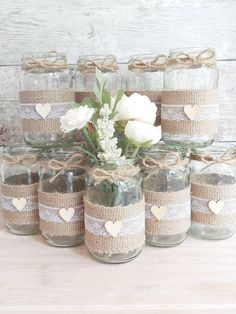 mason jars filled with flowers and hearts tied in twine to each other on a wooden table