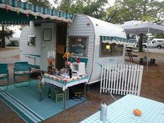 a camper trailer is set up with picnic tables and chairs