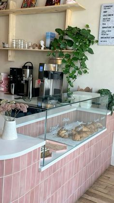 a bakery counter with pastries and coffee machines in the back ground, behind which is a pink tiled wall