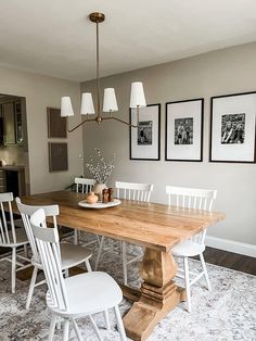 a dining room table with white chairs and pictures hanging on the wall above it,