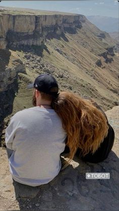 a man and woman sitting on top of a cliff