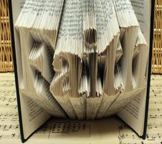 an open book with pages folded into the shape of letters on top of sheet music