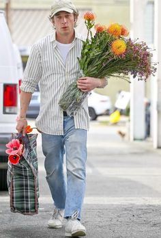 a man is walking down the street with flowers in his hand and holding a shopping bag