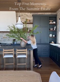 a woman standing in a kitchen next to a counter top with a vase on it