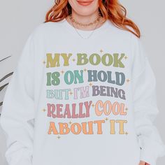 a woman wearing a white sweatshirt that says, my book is on hold but i'm being really cool about it