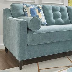 a blue couch sitting on top of a wooden floor next to a white rug and window