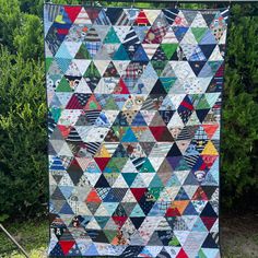 a quilt hanging on a clothes line in front of some trees and bushes with the words,