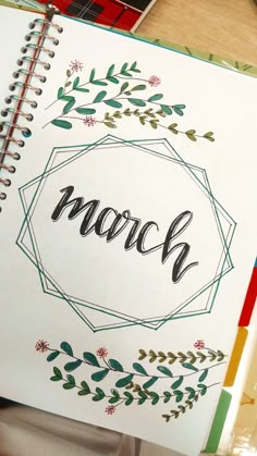 an open notebook with the word march written in cursive writing on it and surrounded by colorful pencils