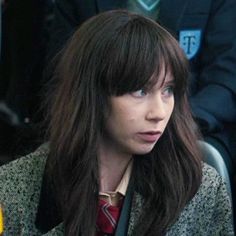 a woman with long hair wearing a suit and tie sitting in front of other people