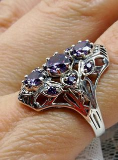 Art Deco 1930s Amethyst 9-Gem Ring9Gem Ring Design#D69 Give your wardrobe the stylish edge it needs with the Amethyst 9-Gem Ring. This stunning vintage Art Deco ring is crafted from sterling silver, making it just as timeless as its design. The piece is set with three captivating center 6mm round cut Purple/Amethyst CZ gemstones and six more 2mm gemstones that adorn the sides of the setting. A unique filigree silver band completes this work of art to perfections - an impressive reminder of the g Vintage Purple Sapphire Gemstone Ring, Vintage Amethyst Ring With Accent Stones, Vintage Amethyst Ring With Accent Stones For Collectors, Art Deco Amethyst Round Ring, Purple Anniversary Rings With Intricate Design, Vintage Amethyst Ring With Accent Stones For Anniversary, Art Deco Purple Amethyst Ring For Anniversary, Vintage Purple Amethyst Ring For Anniversary, Purple Amethyst Art Deco Ring For Anniversary