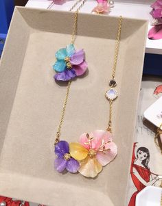 two necklaces with flowers on them are in a box next to other jewelry items