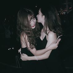 two young women hugging each other in the dark at an outdoor event, one is wearing a black dress and the other has long brown hair