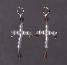 a pair of cross shaped earrings with red and white beads hanging from it's earwires