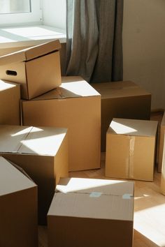 many cardboard boxes are stacked on the floor in front of a window with sunlight streaming through them