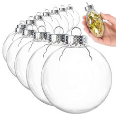 a hand holding an ornament in front of five clear glass baubles