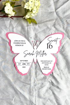 a pink and white butterfly on a piece of paper with flowers in the back ground