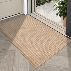 a door mat on the floor in front of an open door with a potted plant next to it