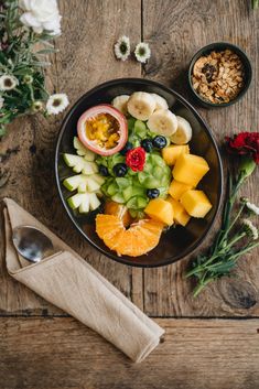 a bowl filled with fruit on top of a wooden table next to flowers and spoons