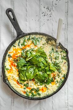 a skillet filled with rice and spinach on top of a white table cloth