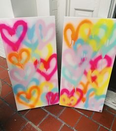 two canvases with hearts painted on them sitting in front of a white door and brick floor