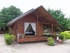 a small wooden cabin sitting on top of a sandy beach next to green bushes and trees