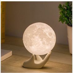 a white moon lamp sitting on top of a table next to a potted plant