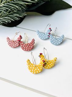 three pairs of polka dot bird earrings sitting on top of a white table next to a plant